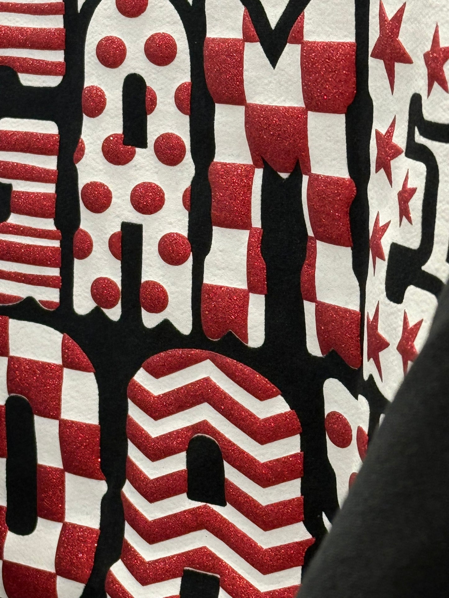 A close-up of a red, white, and black patriotic-themed graphic design featuring glittery red stars, stripes, polka dots, and chevron patterns on stylized letters.