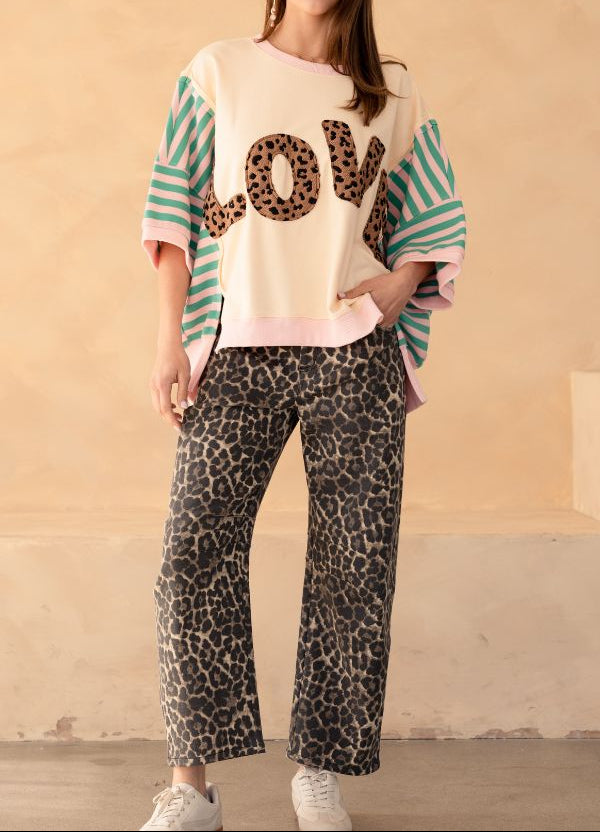 Woman wearing a sweater with 'LOVE' print and leopard print pants against a beige background