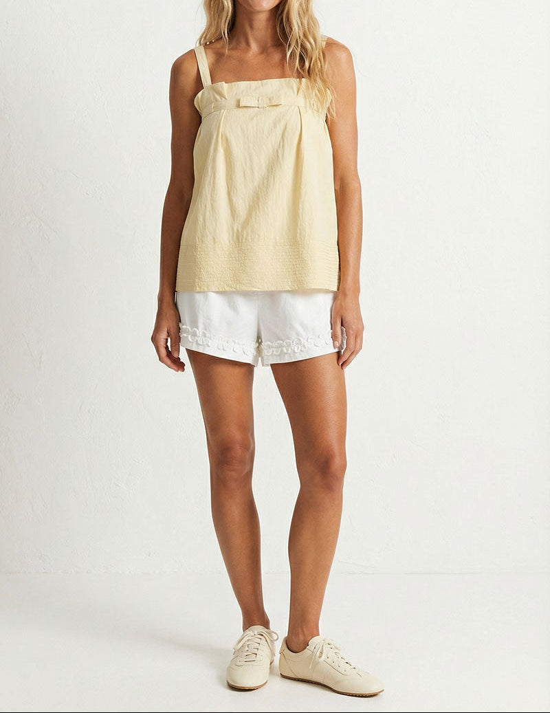 Woman wearing a light yellow sleeveless top and white shorts on a white background