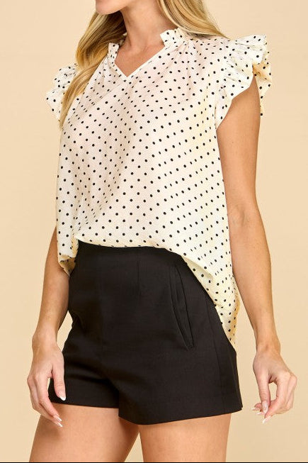 Woman wearing a polka dot blouse and black shorts on a beige background