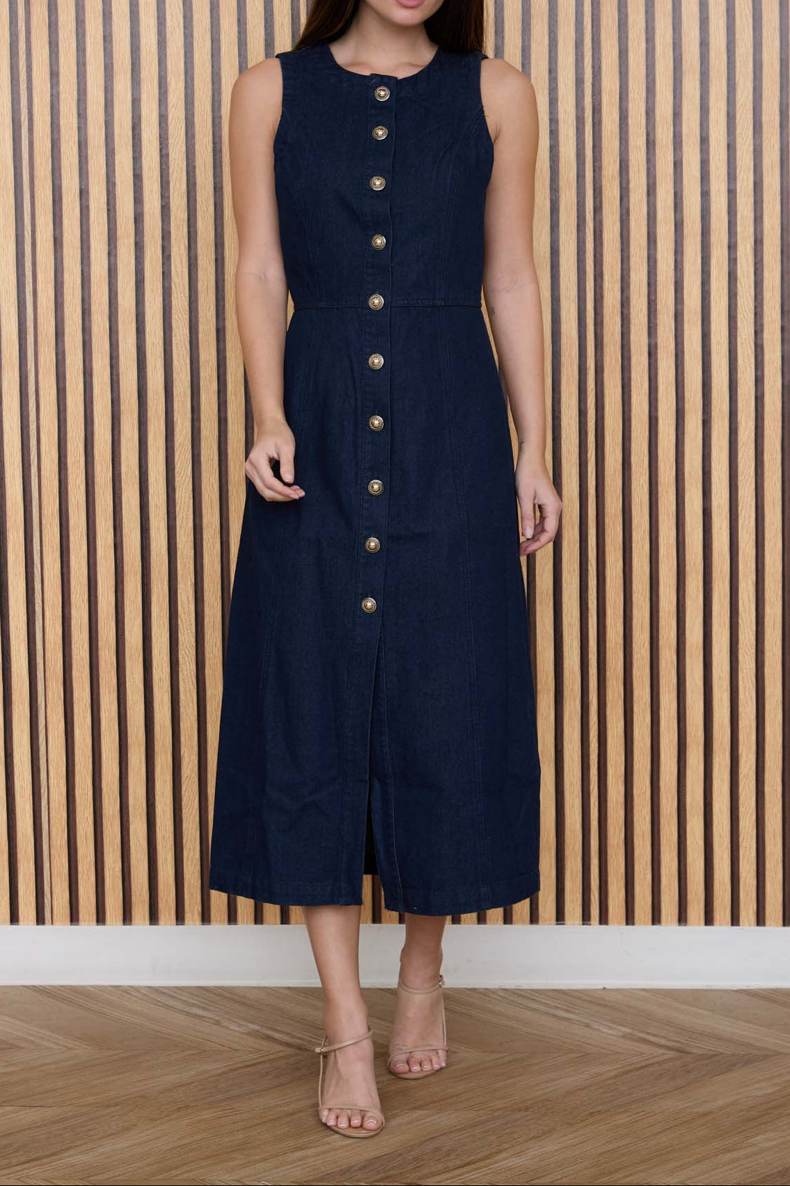 Woman wearing a navy dress with gold buttons against a wooden paneled wall.