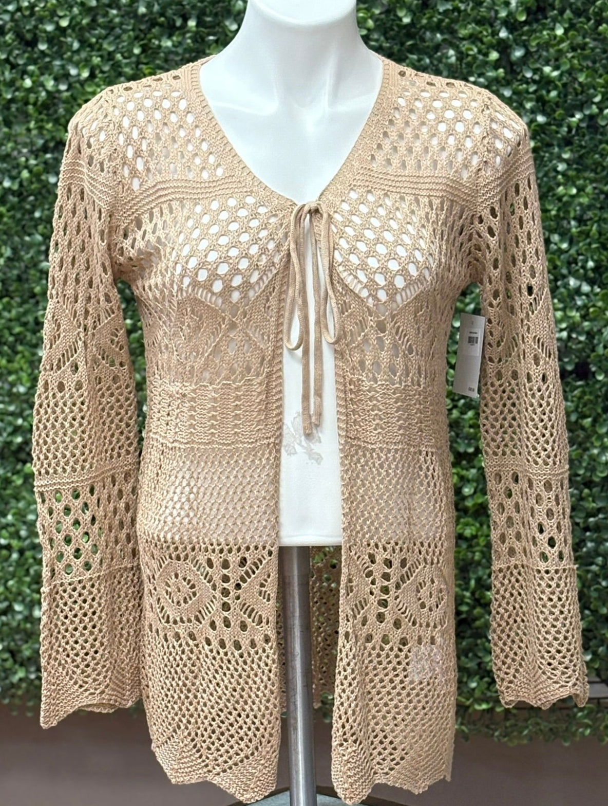 Tan crochet top on a mannequin against a green leafy background