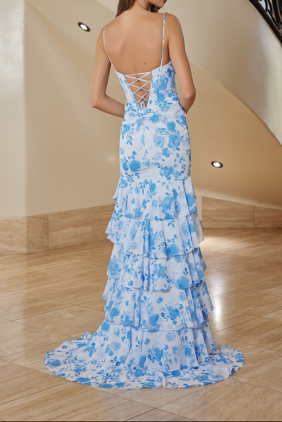 Woman in a blue floral evening gown standing in a elegant interior setting.
