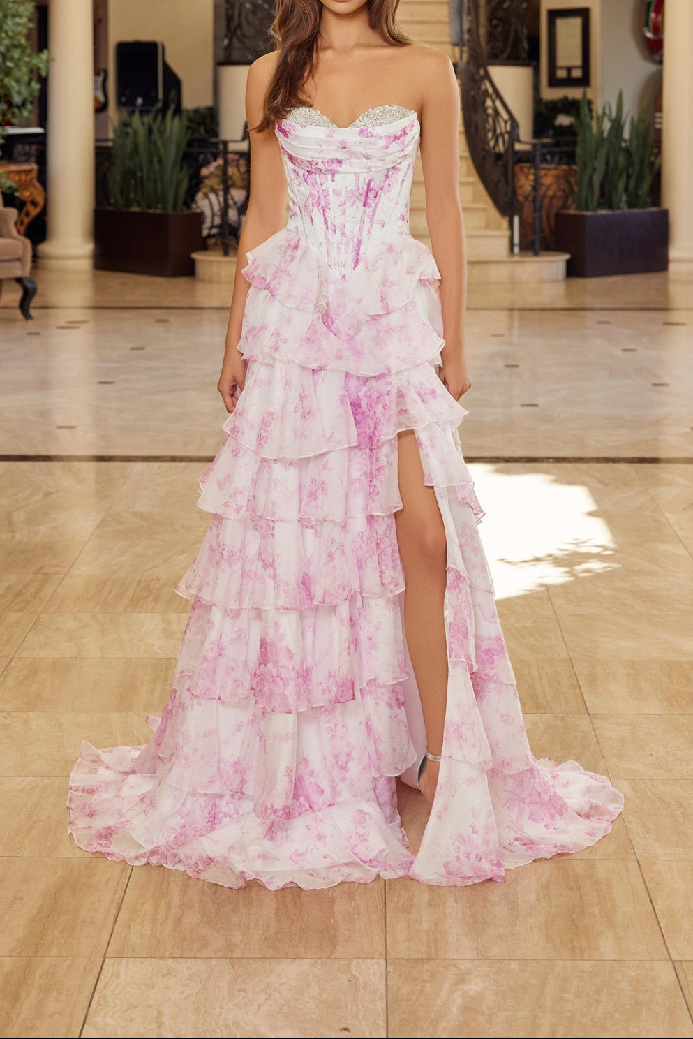 Woman in a pink floral dress standing in a elegant indoor setting with chandelier.