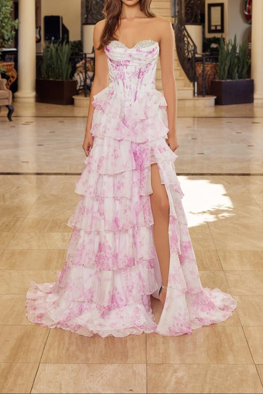 Woman in a pink floral dress standing in a elegant indoor setting with chandelier.