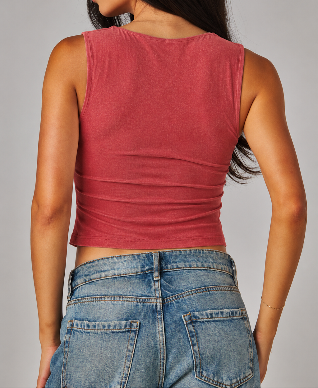 Woman wearing a red tank top and blue jeans against a gray background