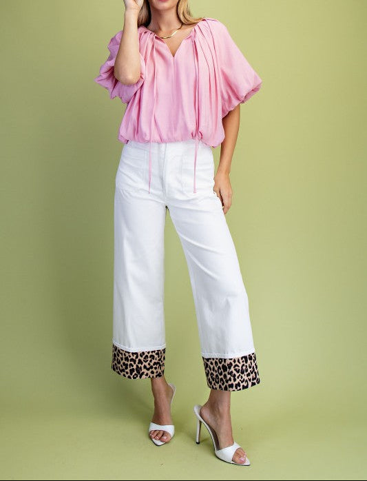 Woman wearing a pink blouse and white pants with leopard print cuffs on a green background