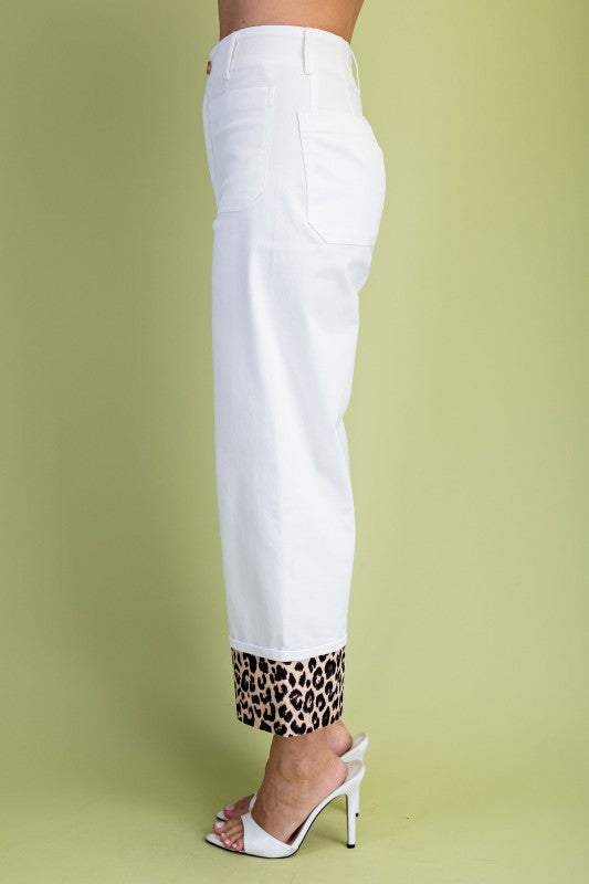 White cropped jeans with a leopard print hem, shown on a model from the side against a light green background.