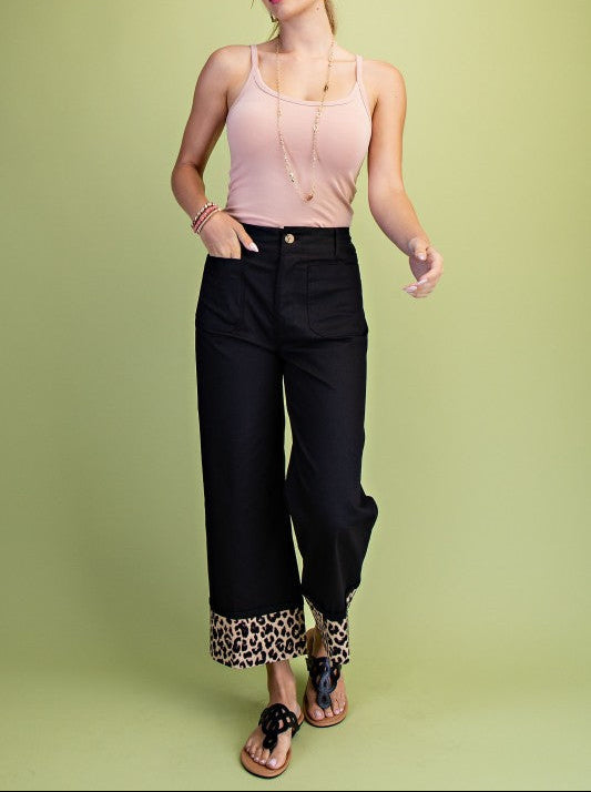 Woman wearing a pink top and black pants with leopard print cuffs on a green background