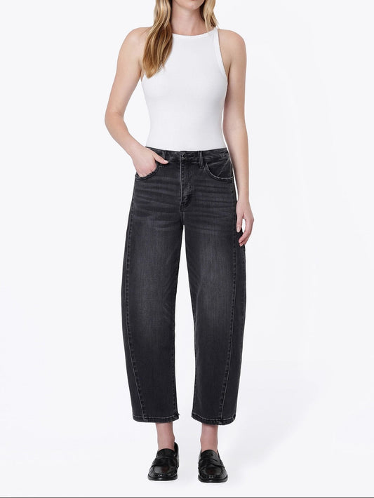 A woman modeling a pair of wide-leg cropped black jeans with a white sleeveless top and black loafers, standing against a plain white studio background.