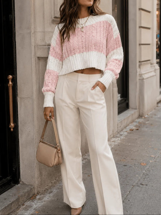 Woman wearing a pink and white striped sweater and white pants, standing on a city street.