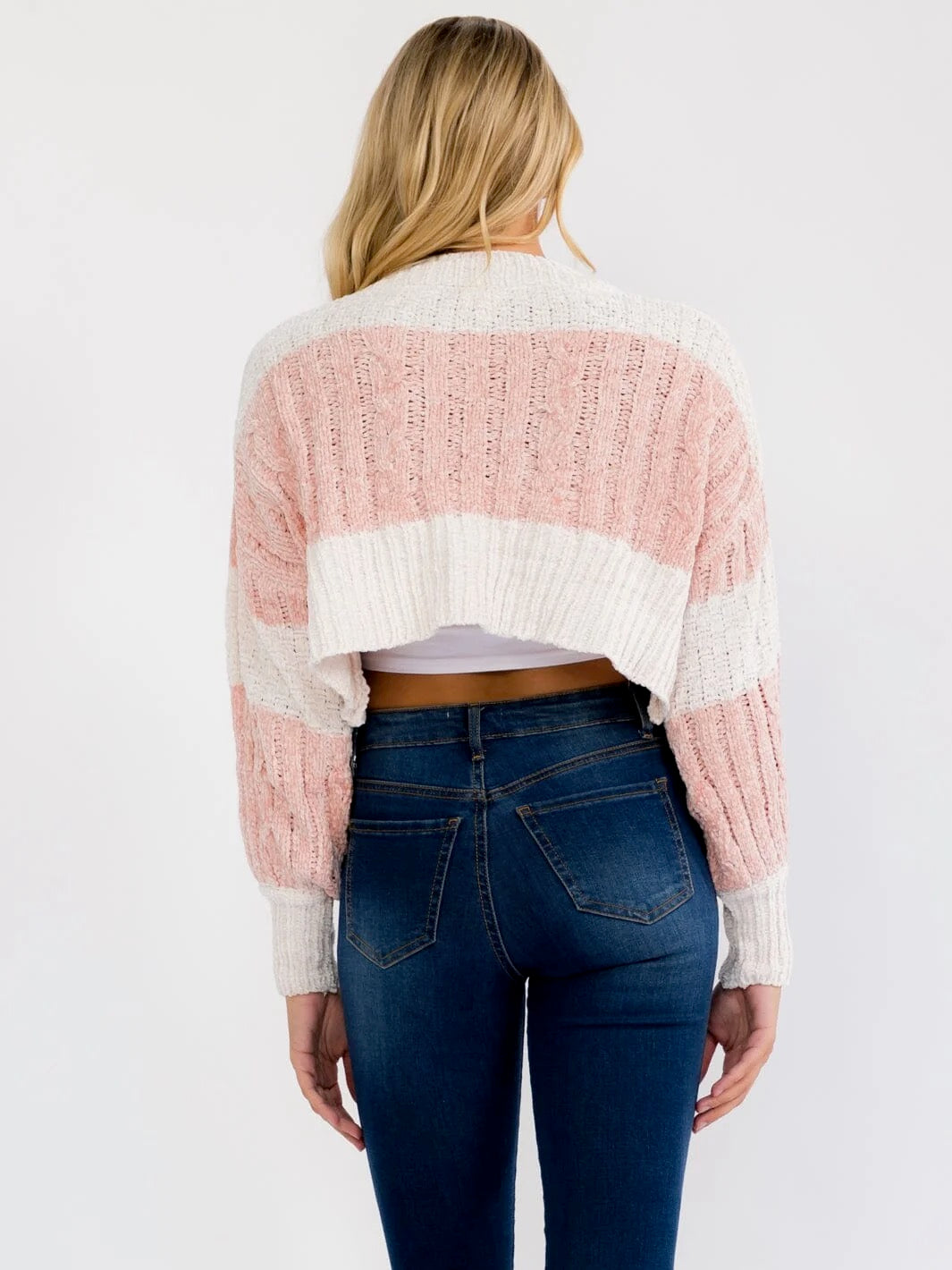 A woman shown from the back wearing a pink and off-white striped cropped knit sweater and dark blue jeans against a plain white background.