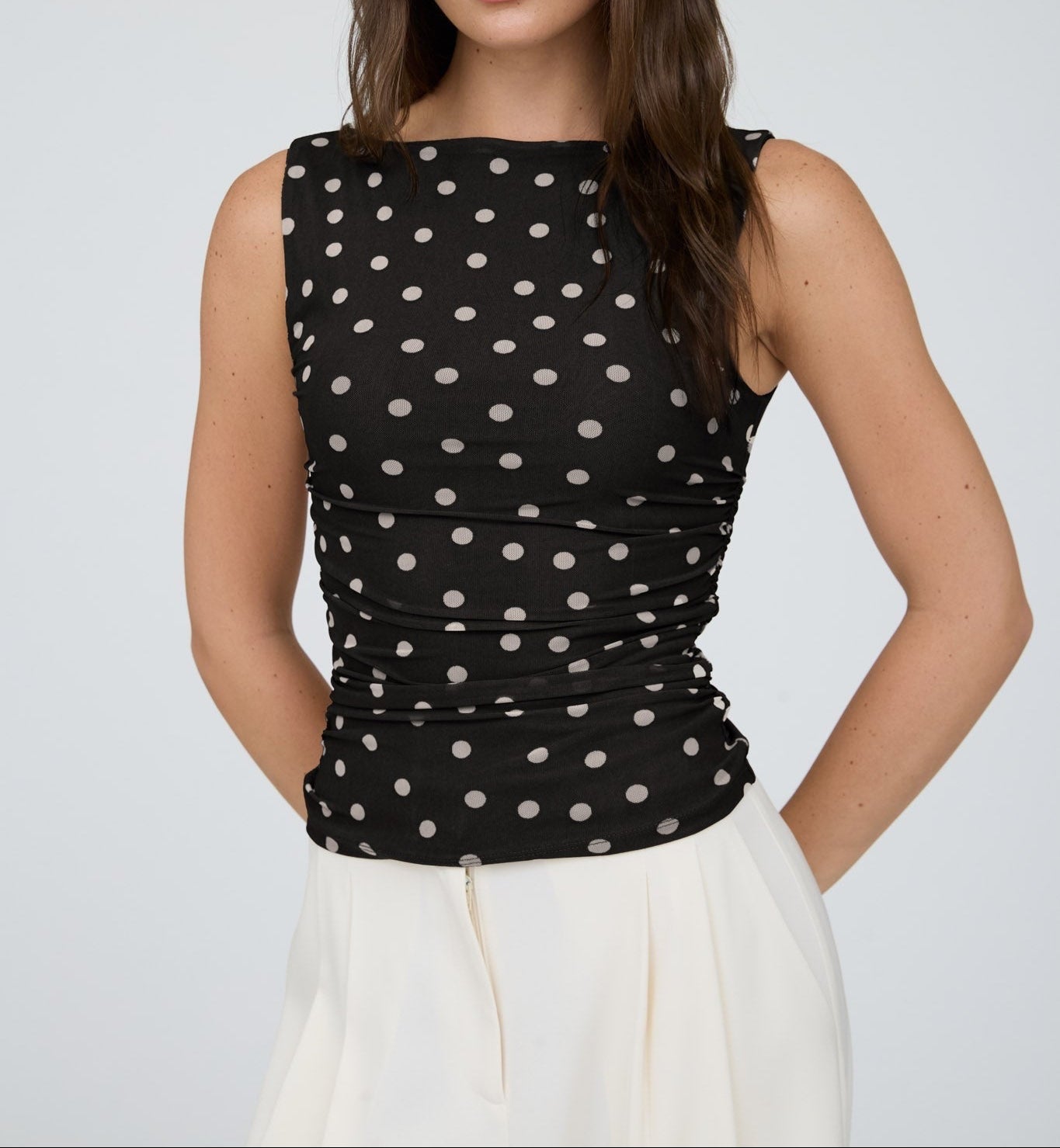 Woman wearing a black sleeveless top with white polka dots against a plain background