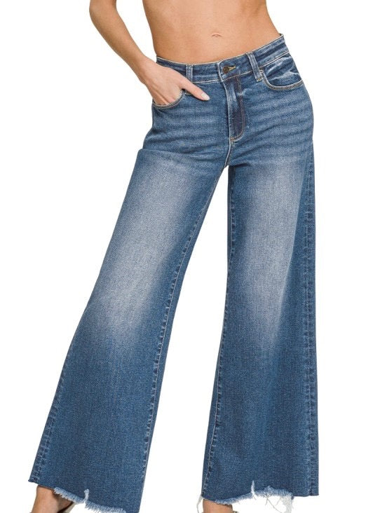 A person wearing blue wide-leg denim jeans with a frayed hem, shown from the waist down against a plain white background.
