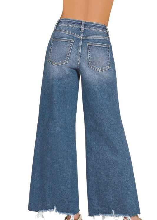 Wide-leg blue denim jeans shown from the back on a model, featuring a high waist, back pockets, and a raw frayed hem.