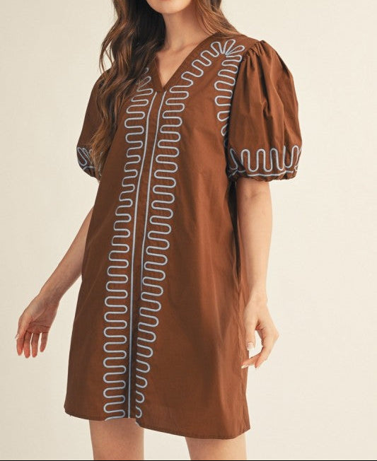 Woman wearing a brown dress with decorative patterns on a beige background