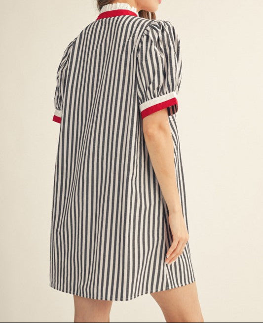 A woman wearing a short-sleeve striped shirt dress, shown from the back. The dress features vertical black and white stripes with red and white trim on the collar and sleeve cuffs.
