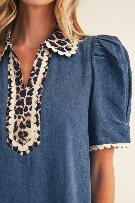 Close-up of a blue short-sleeve blouse with a leopard-print and cream scalloped collar and placket, worn by a model.