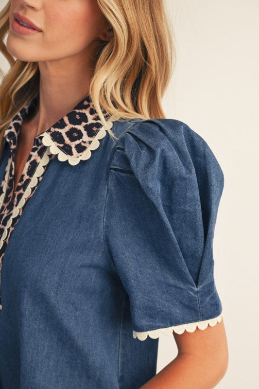 Close-up of a woman wearing a blue denim blouse with a large leopard-print scalloped collar and matching scalloped trim on the sleeves.