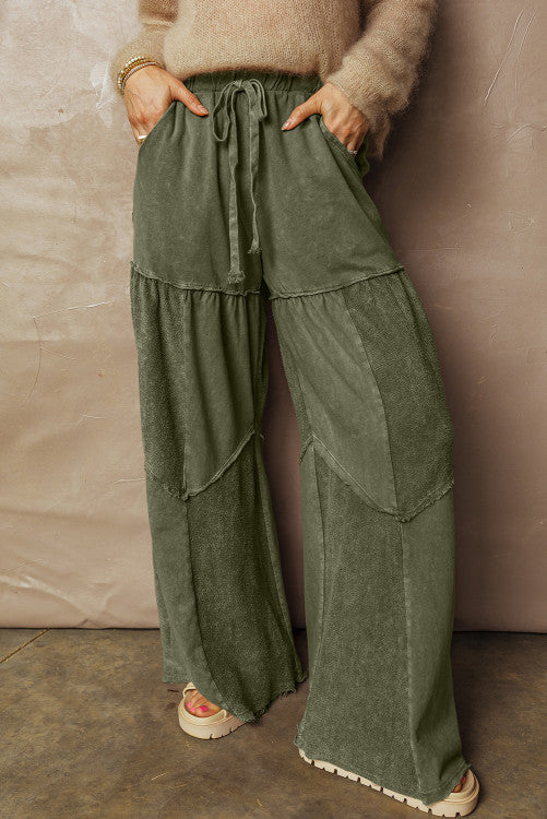 Person wearing green layered pants against a beige wall.