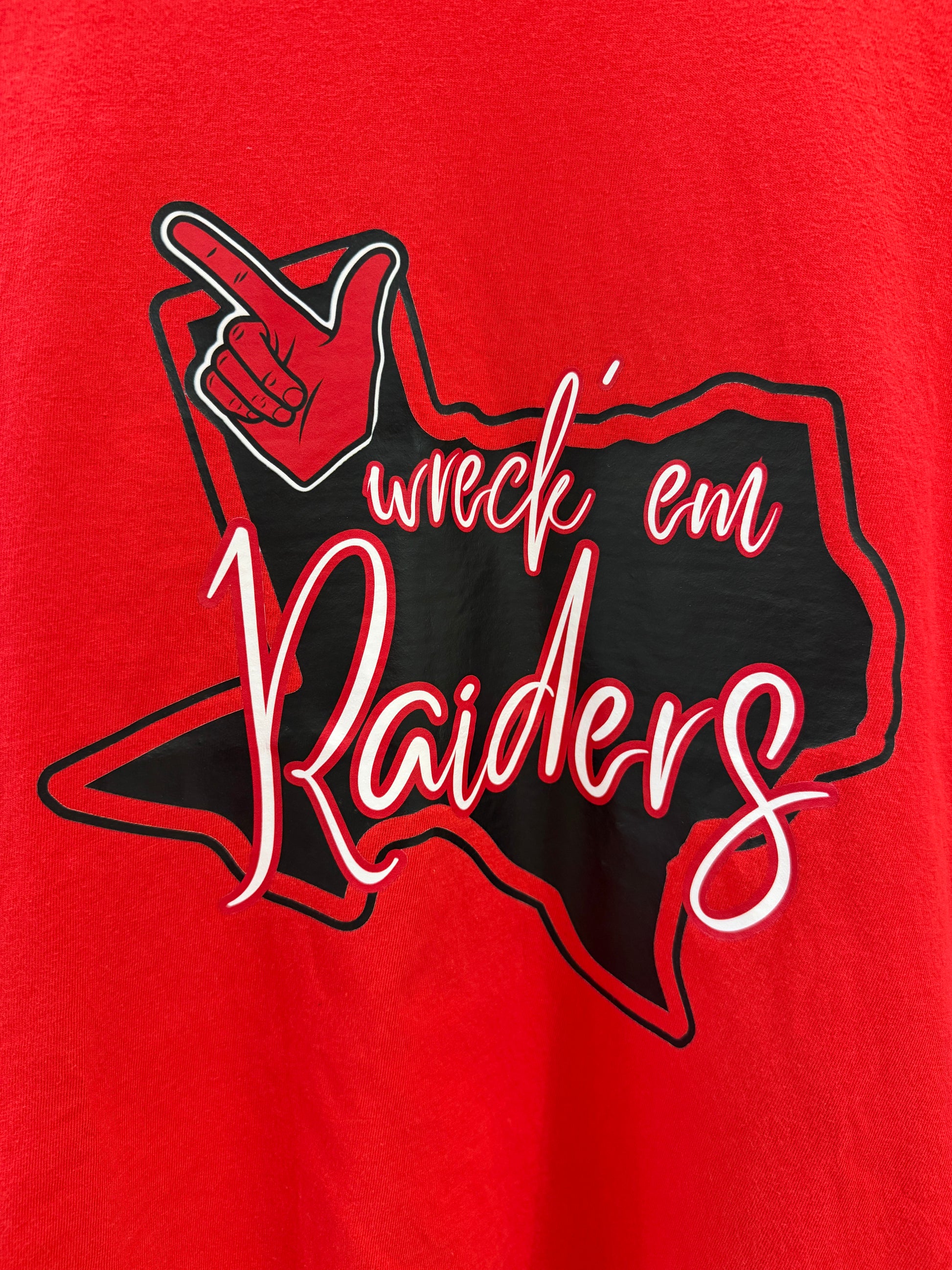 A close-up of a red graphic print featuring a black silhouette of Texas with the words 'wreck 'em Raiders' in white script with a red outline, plus a hand pointing forward inside the design.