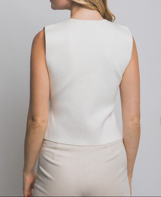 Woman wearing a light-colored sleeveless top and beige pants against a plain background