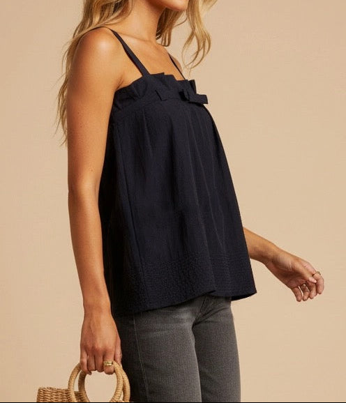 Woman wearing a navy blue top with thin straps against a beige background