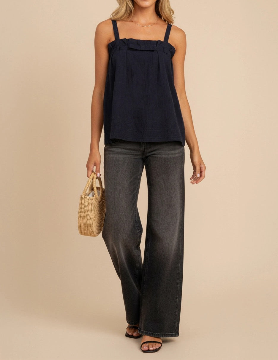 Woman wearing a navy top and dark pants holding a woven bag on a beige background