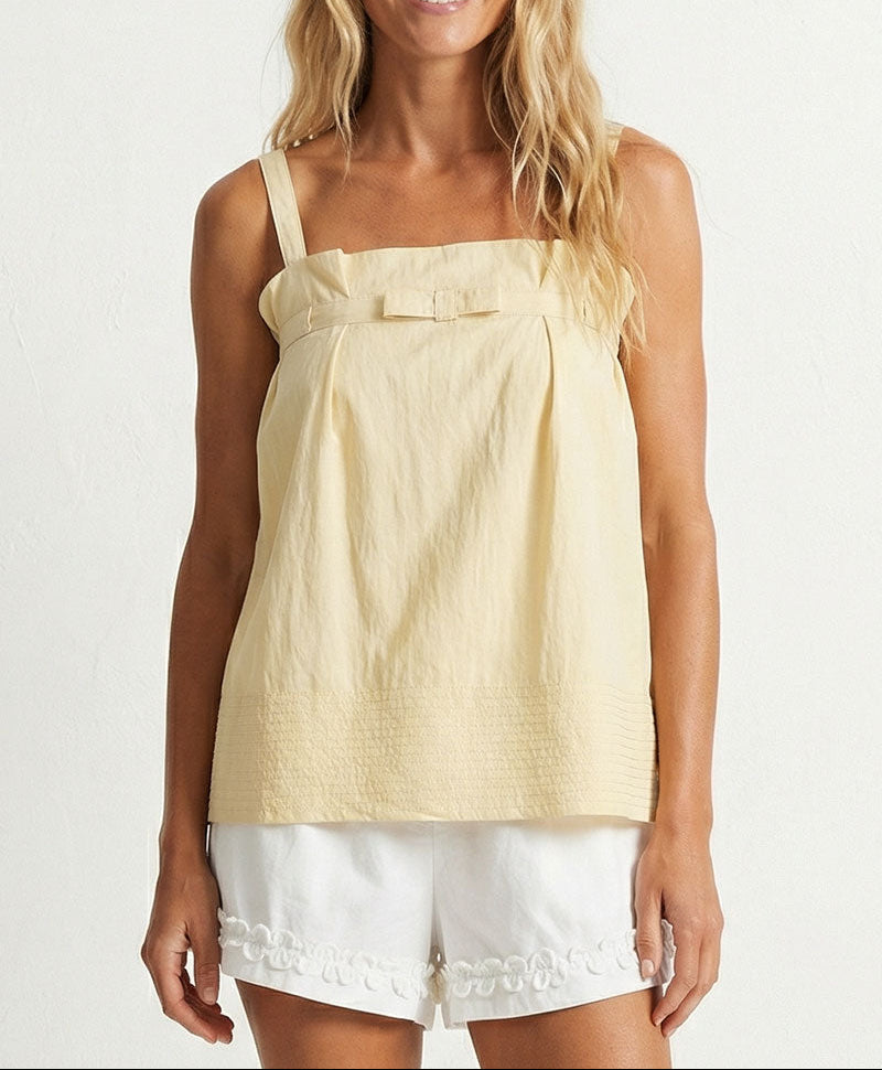 Woman wearing a yellow top and white shorts on a plain background