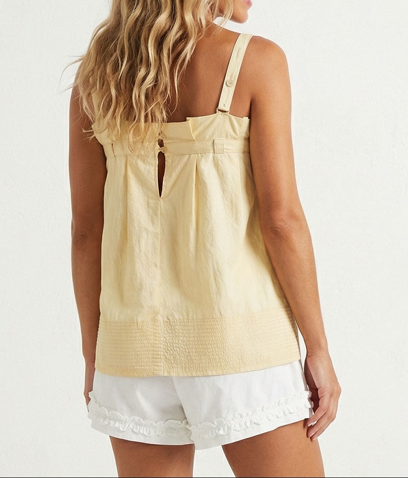 Woman wearing a yellow sleeveless top and white shorts on a plain background