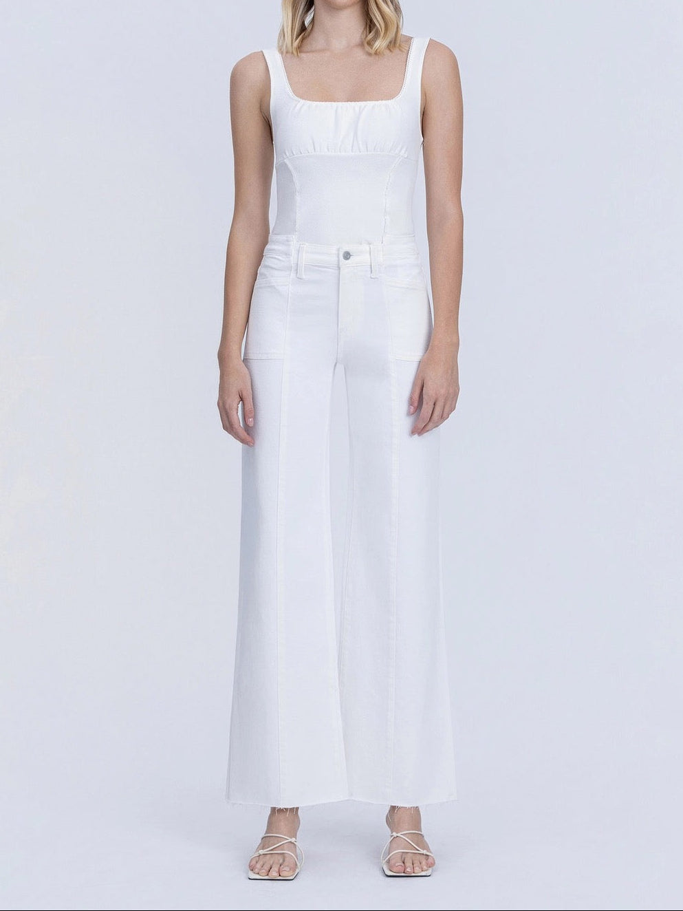 Woman wearing a white sleeveless jumpsuit on a plain background