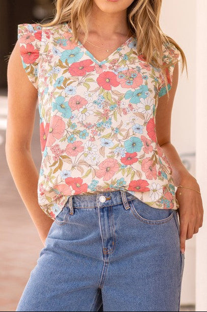 Woman wearing a floral sleeveless top and blue jeans outdoors.