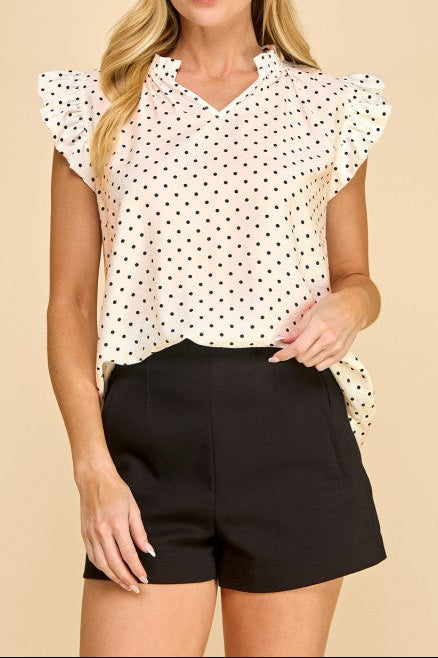 Woman wearing a polka dot blouse and black shorts on a beige background