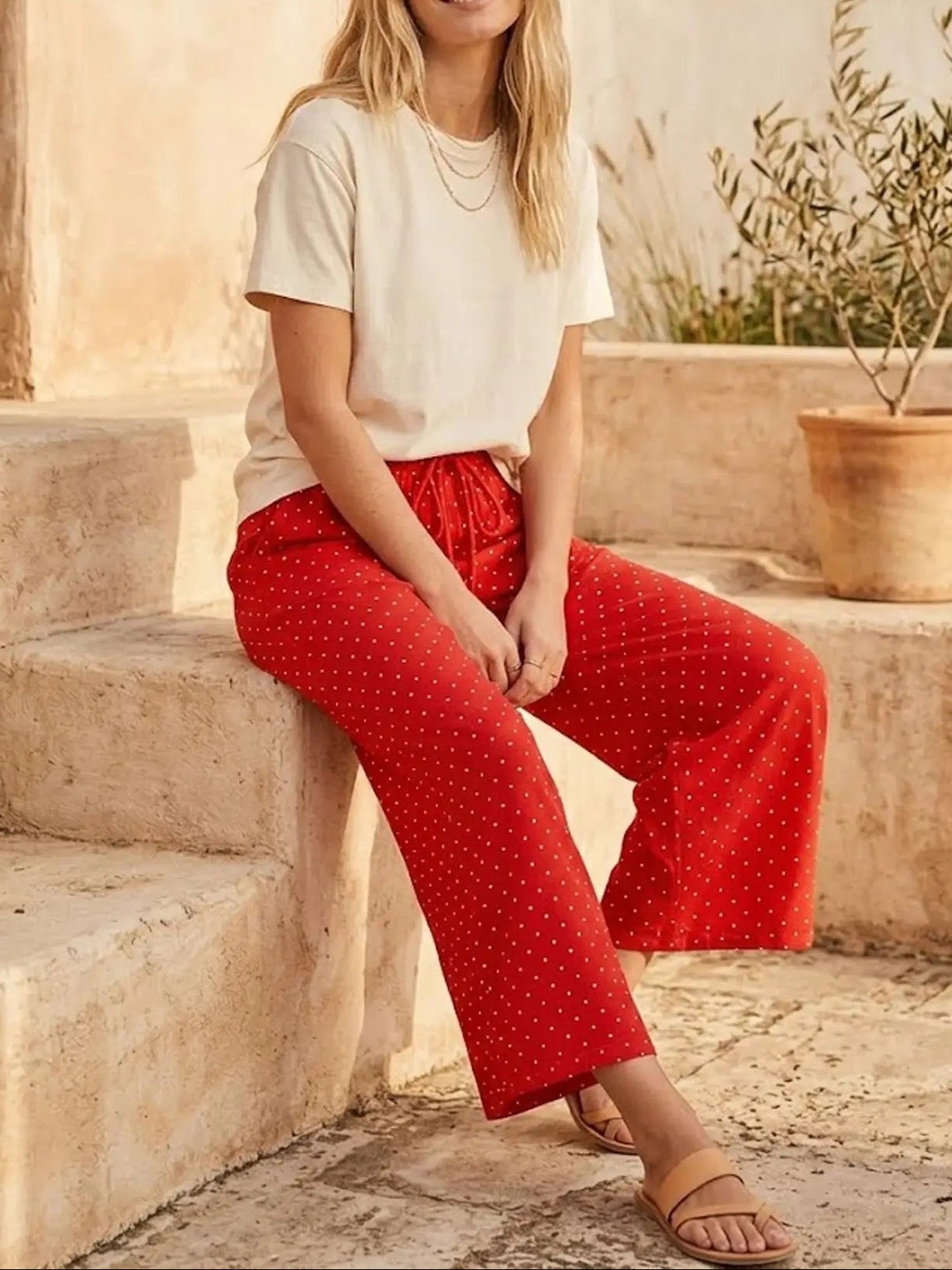 Woman wearing a white top and red polka dot pants sitting on stone steps.