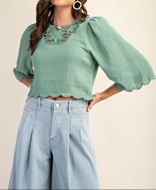 Woman wearing a green blouse with floral embroidery and light blue jeans on a beige background
