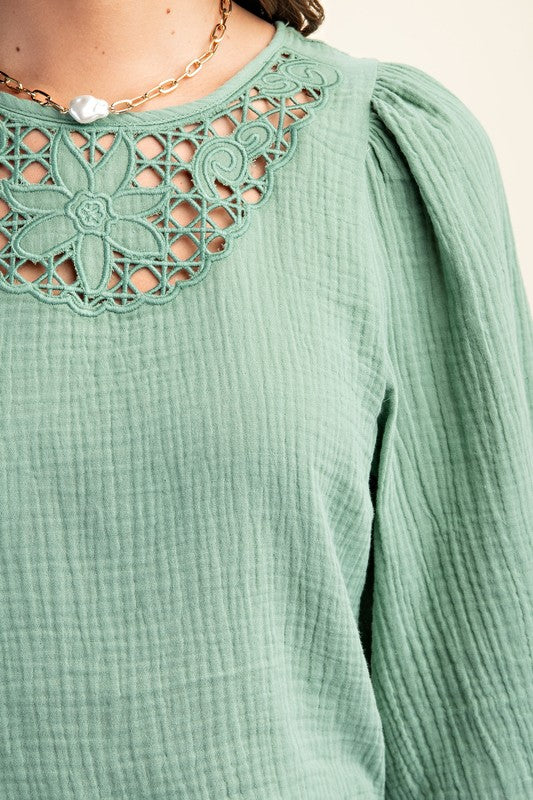 Green textured top with floral lace neckline on a beige background