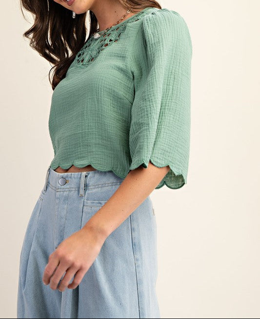 Woman wearing a green top with puffed sleeves and light blue jeans on a beige background
