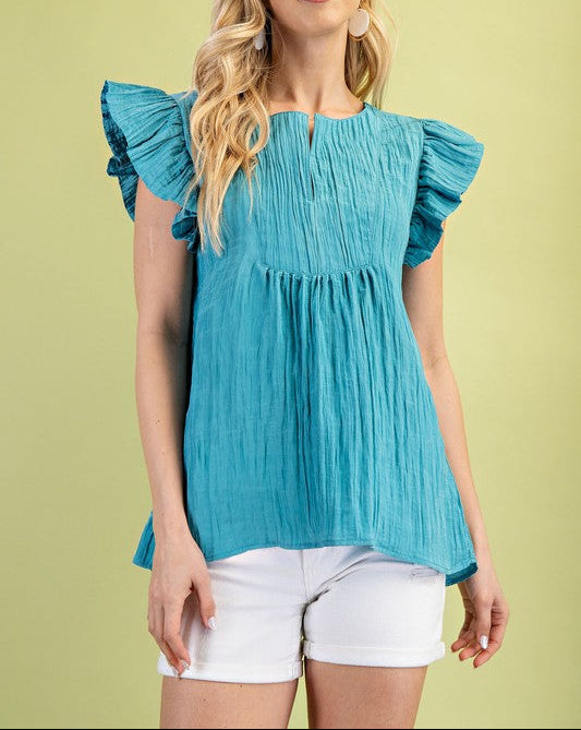 Woman wearing a blue blouse with ruffled sleeves against a light green background