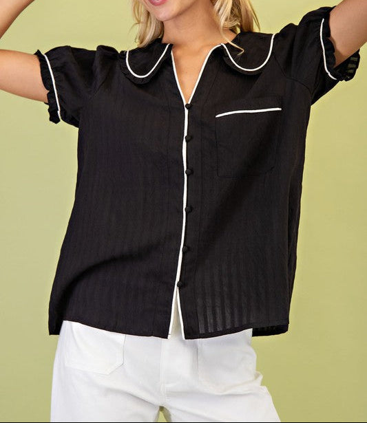 Woman wearing a black short-sleeve blouse with white trim against a green background