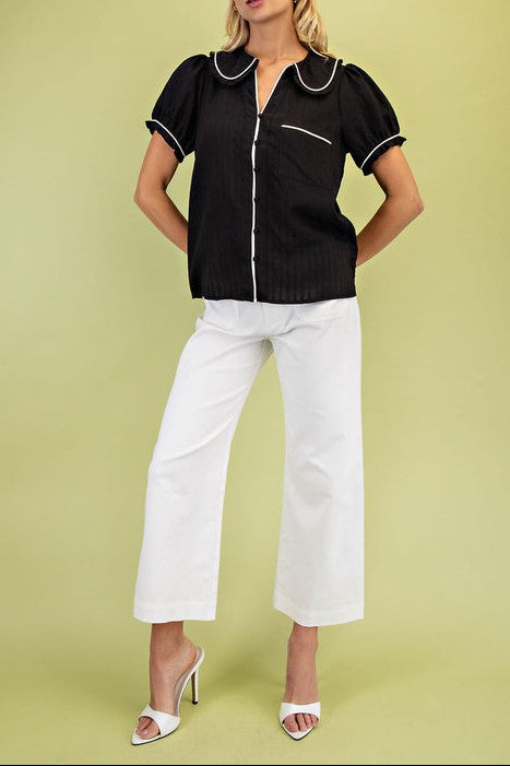 Woman wearing a black top with white trim and white pants on a green background