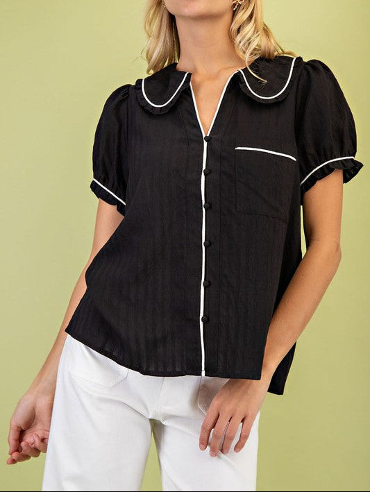Woman wearing a black blouse with white trim against a light green background