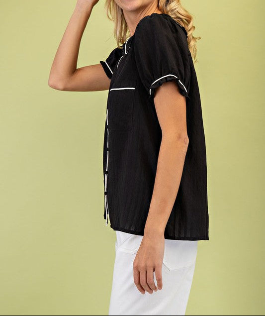 Woman wearing a black top with white trim against a light green background