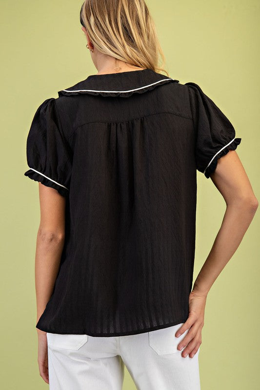 Black blouse with white trim worn by a person on a green background