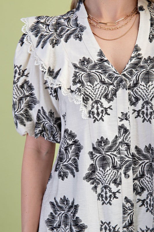 White blouse with black floral pattern on a green background