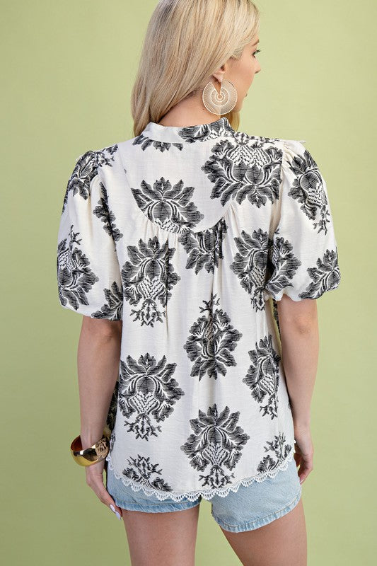 Woman wearing a white blouse with black floral patterns against a green background