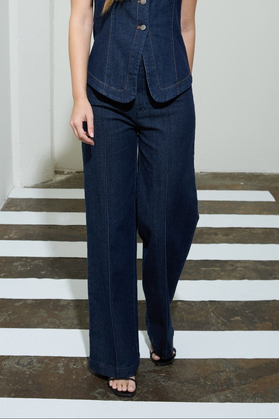 Woman wearing a navy blue sleeveless top and pants standing on a white and gray striped floor.
