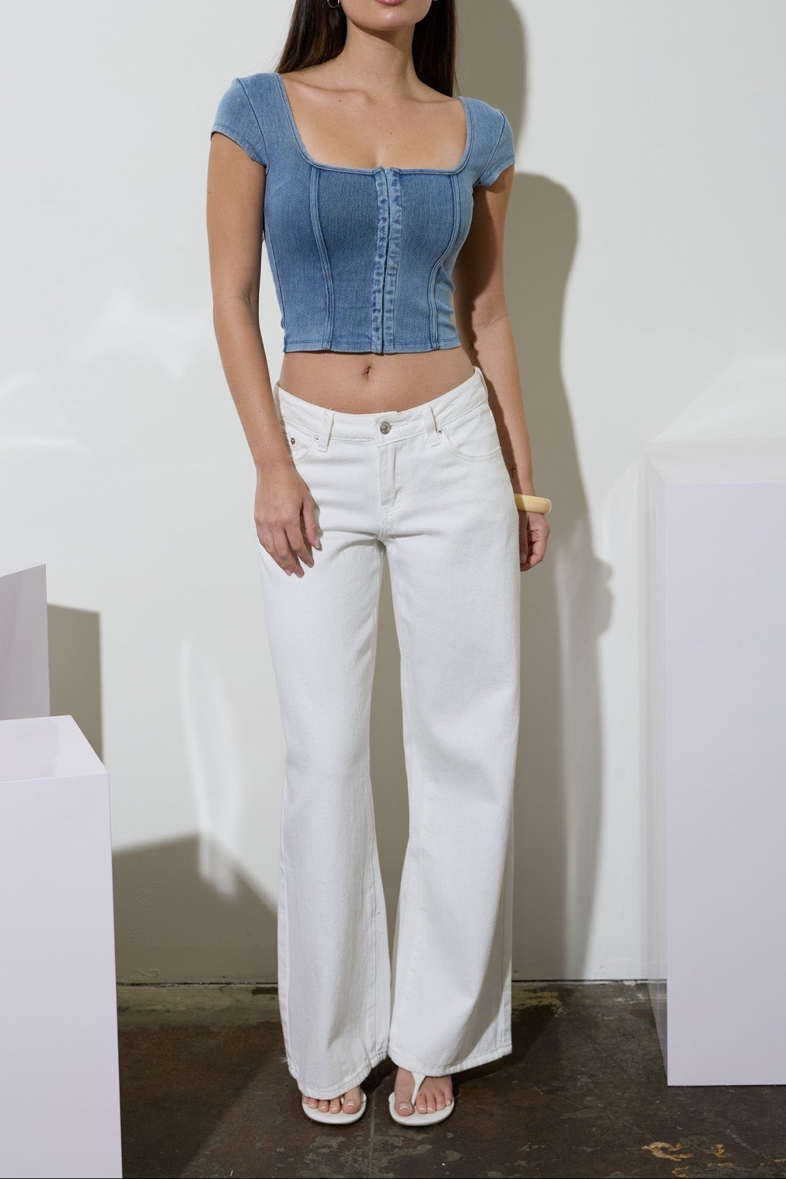 Woman wearing a blue denim top and white pants against a plain background
