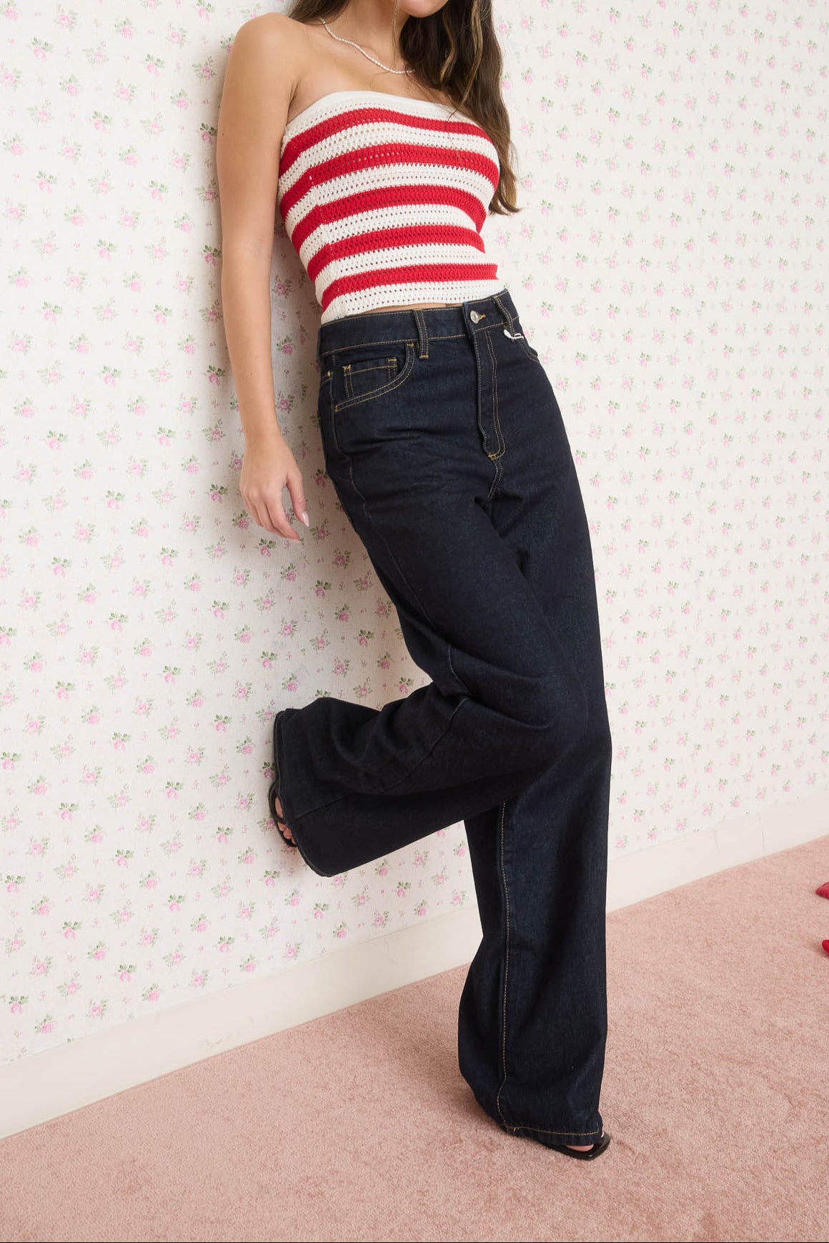 Woman wearing a red and white striped top and dark blue jeans against a patterned wall.