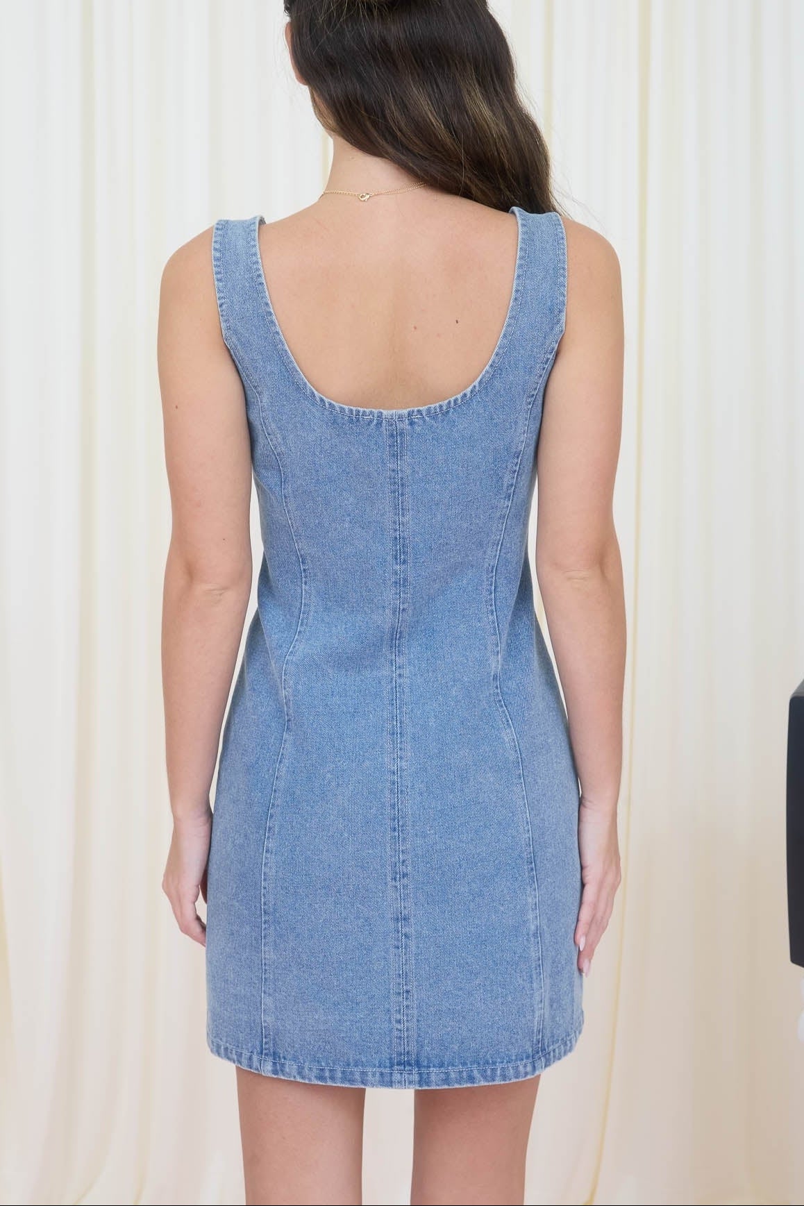 Woman wearing a blue denim dress against a white curtain background