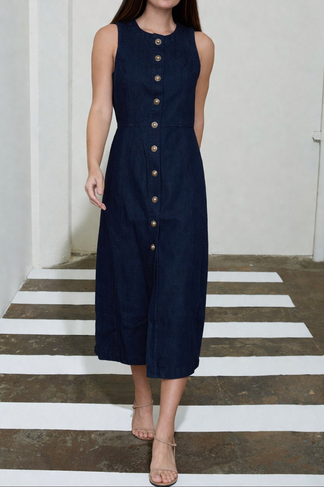 Woman wearing a navy sleeveless dress with buttons on a white and gray striped floor.